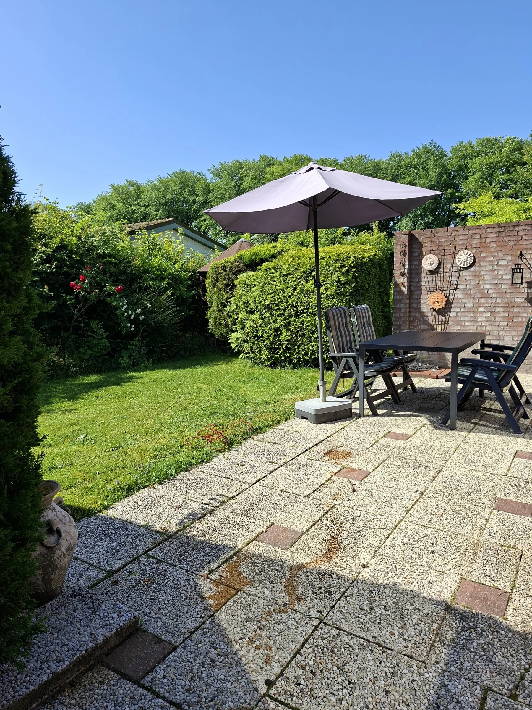 Het terras met tuinset en parasol, omringd door de groene tuin van DuinDromen